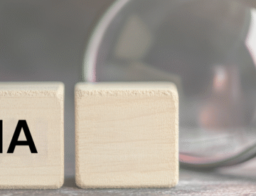 Loupe scrutant les lettres “AI” sur des blocs de bois, représentant l’analyse de l’utilisation de l’intelligence artificielle dans les outils, contenus et processus numériques d’une organisation.